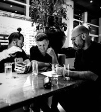 three men sitting at a table talking to each other